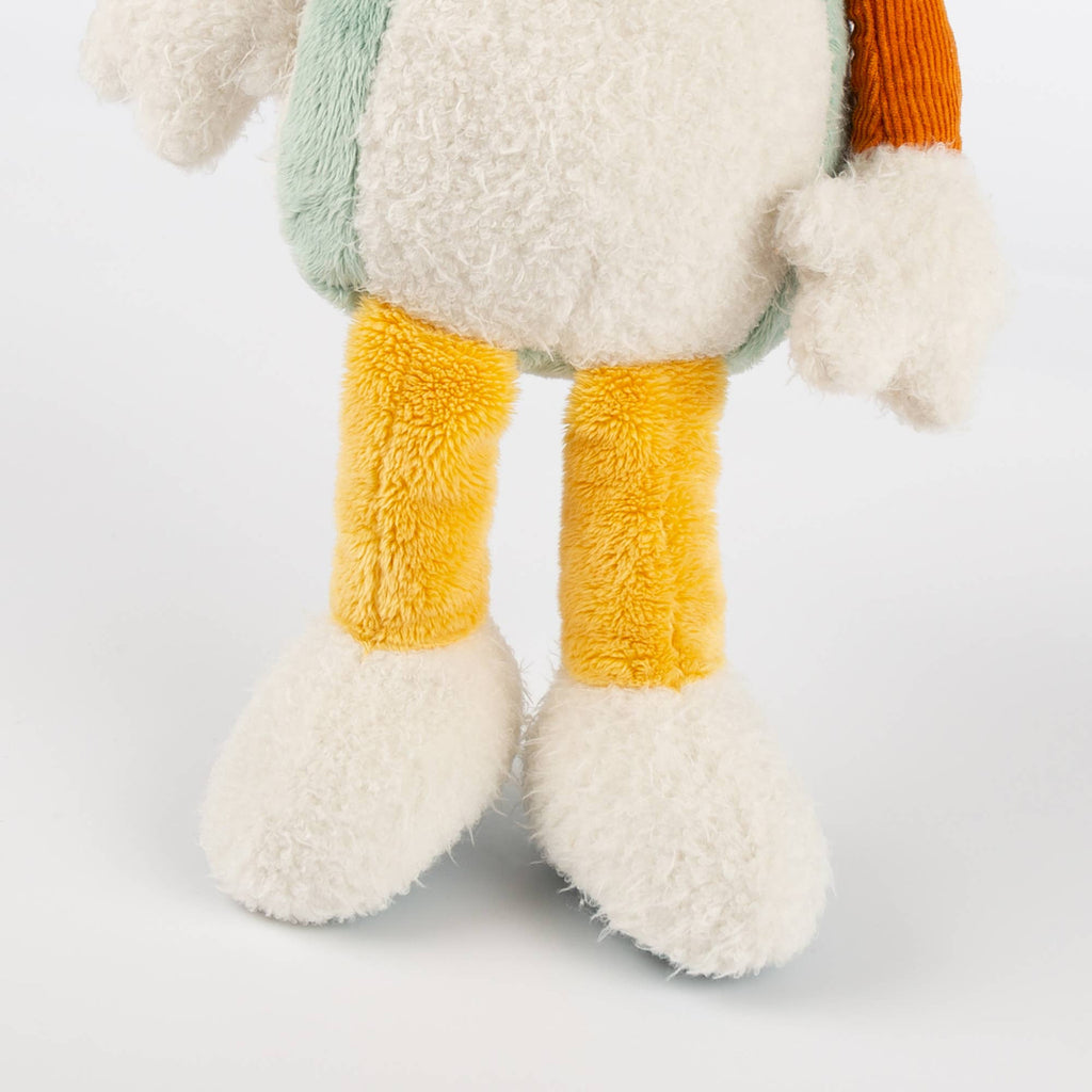 Close-up of a plush toy with yellow legs and white feet on a light gray background