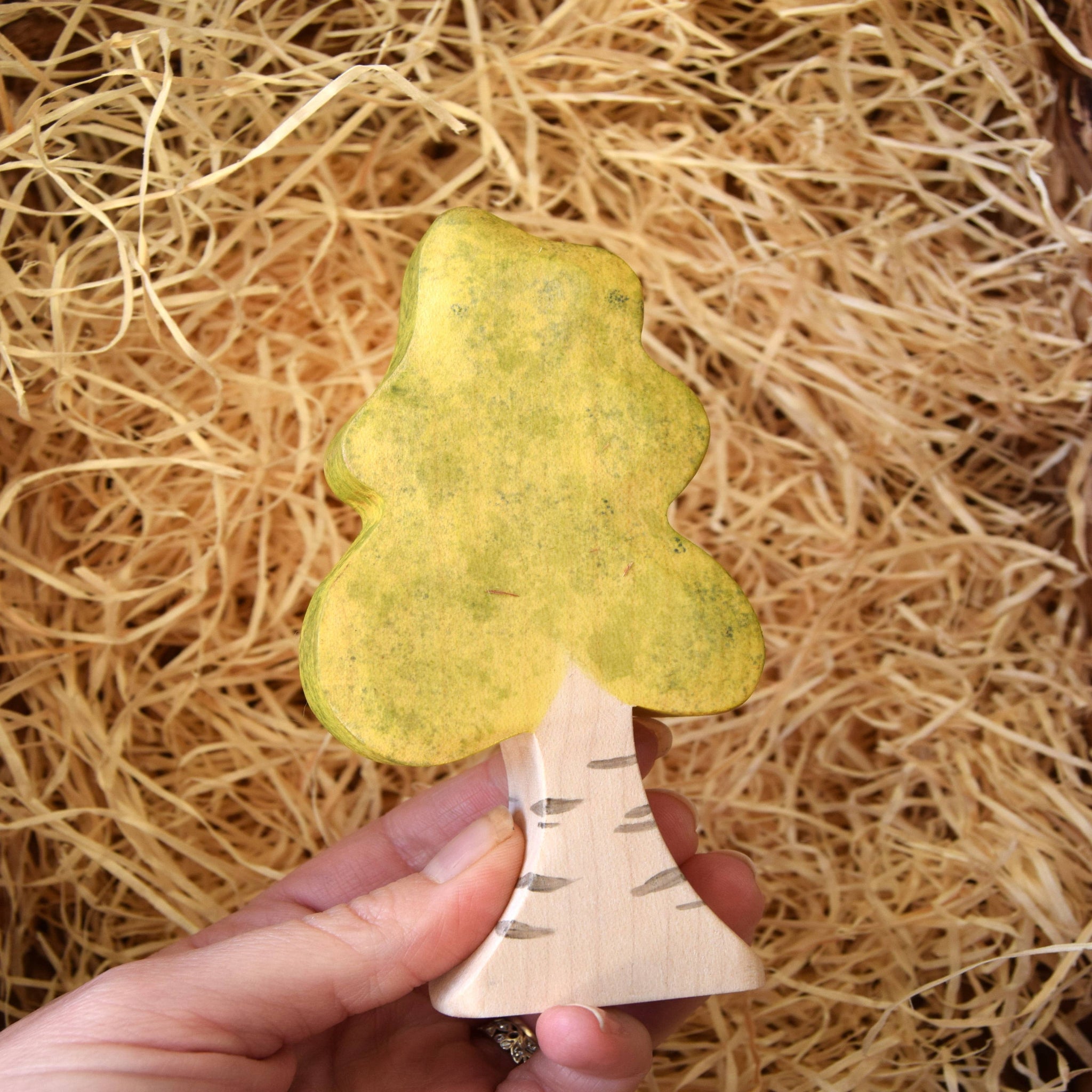 Hand holding a yellow tree-shaped object against a straw background