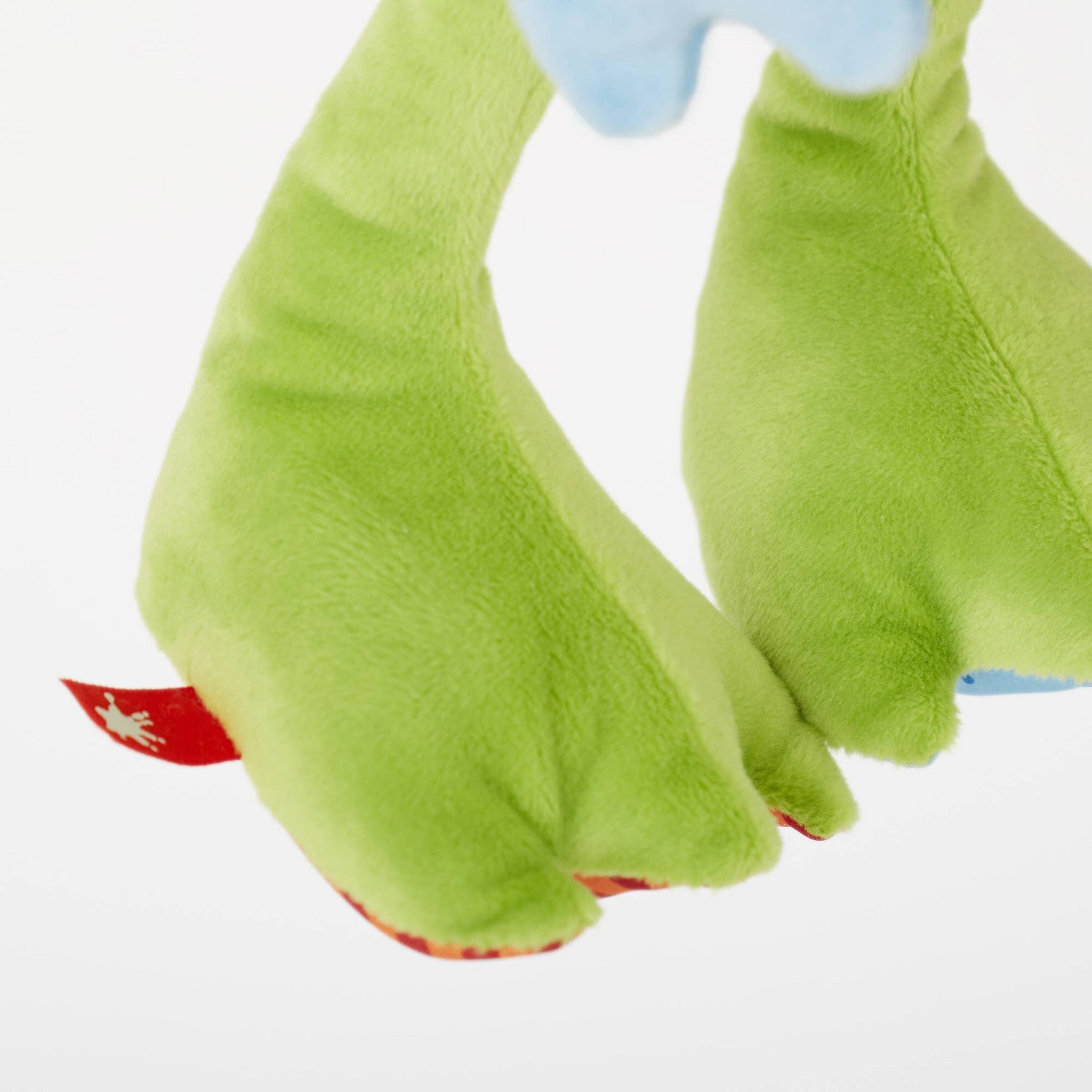 Close-up of green plush toy feet with a red tag on a white background