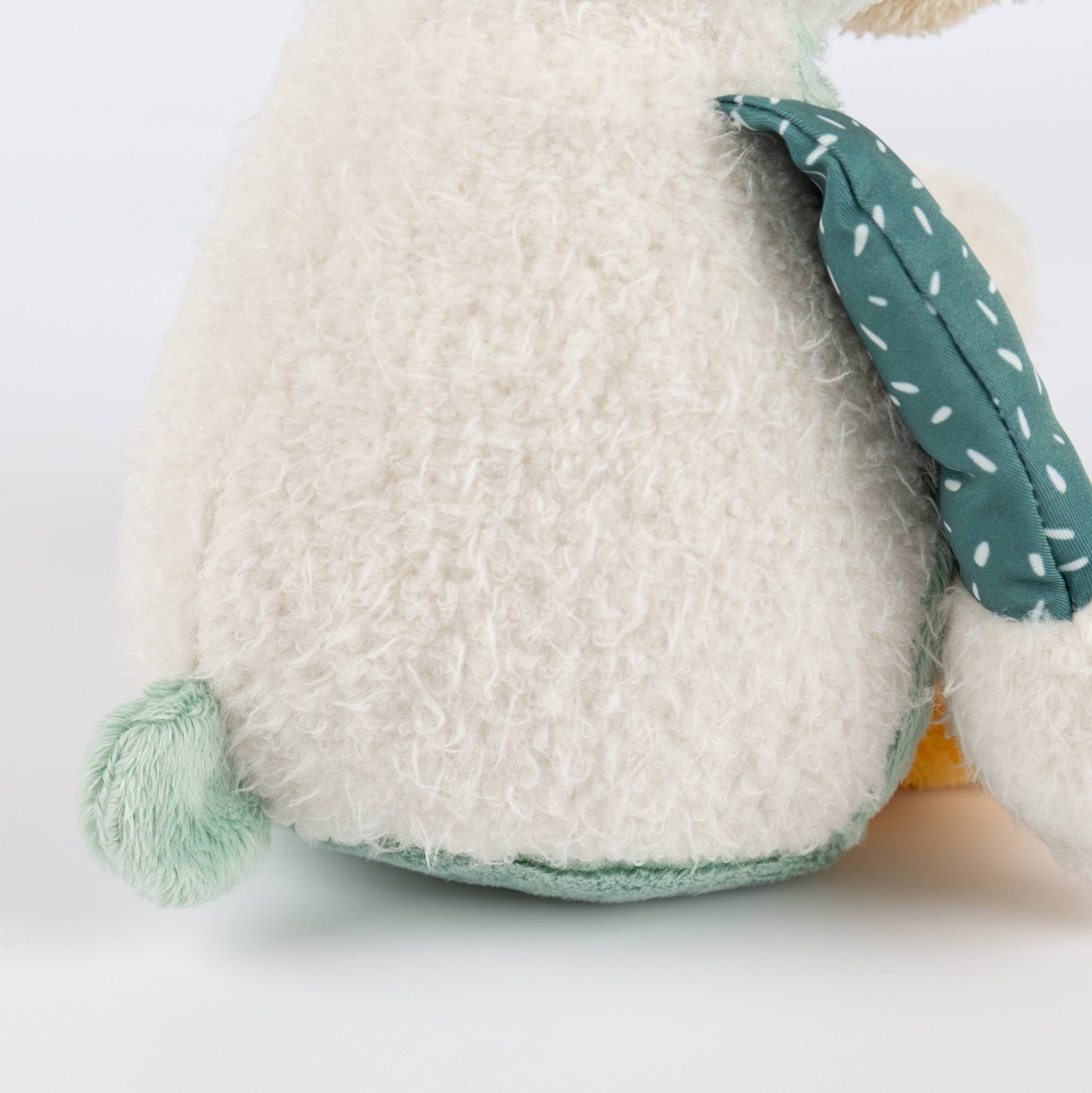 Close-up of a plush toy with a textured white body and green ears on a light gray background