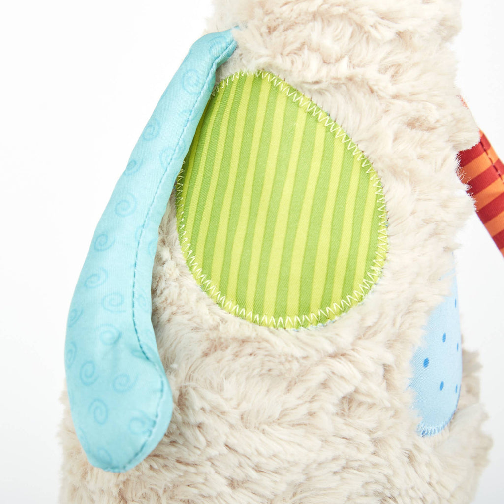Close-up of a plush toy with a textured blue ear and green striped patch on a white background