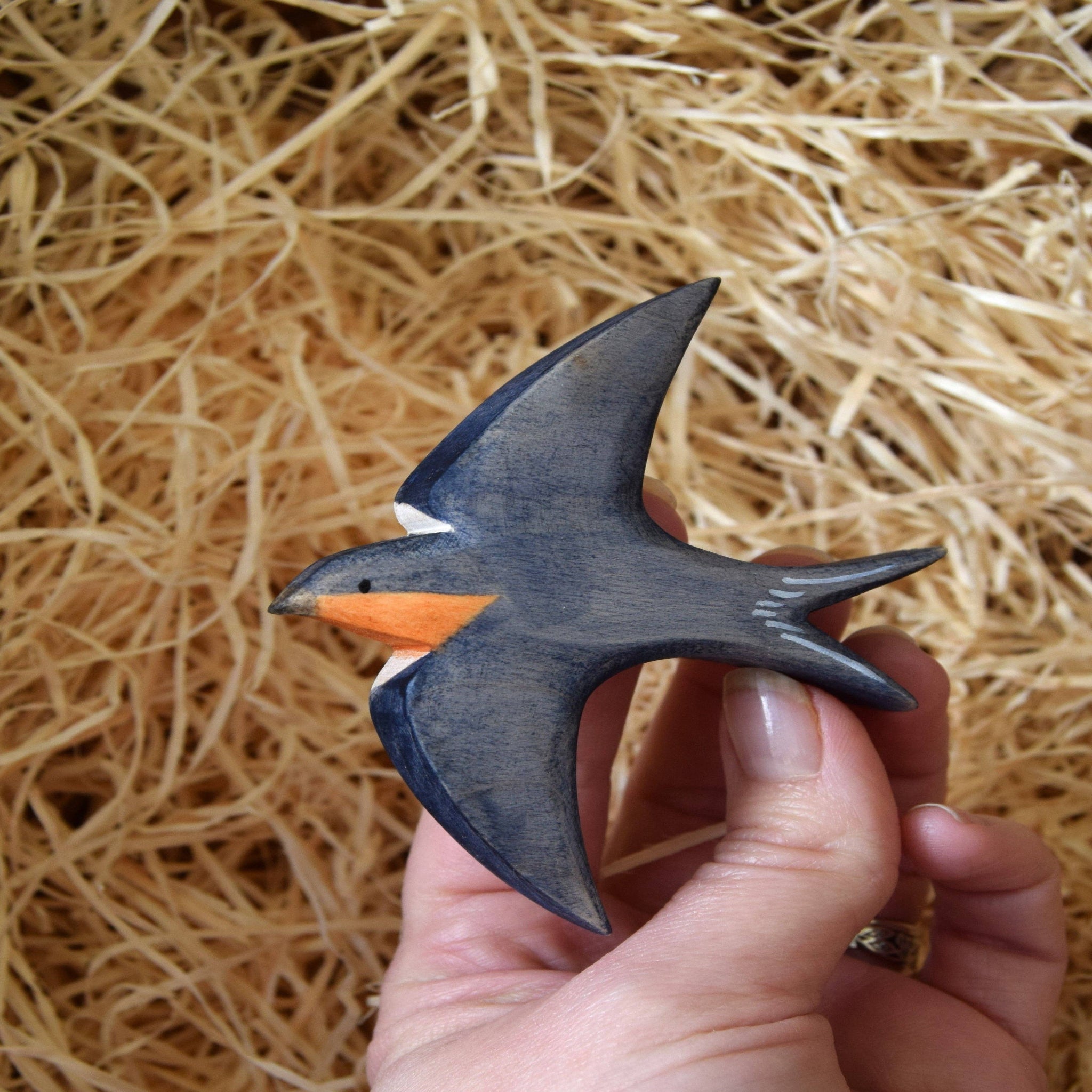 Hand holding a small wooden swallow figurine against a straw background