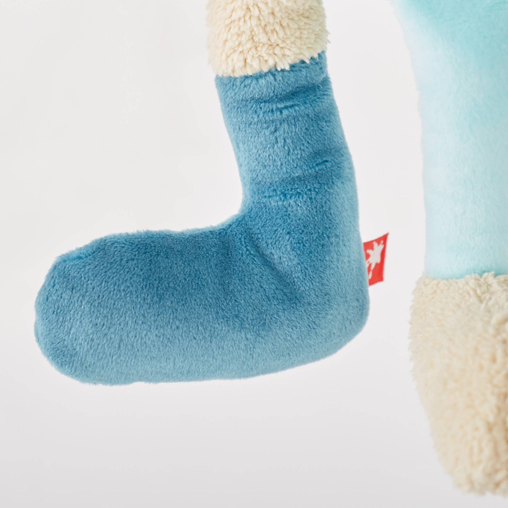 Blue and beige plush toy with a visible brand logo on a light gray background
