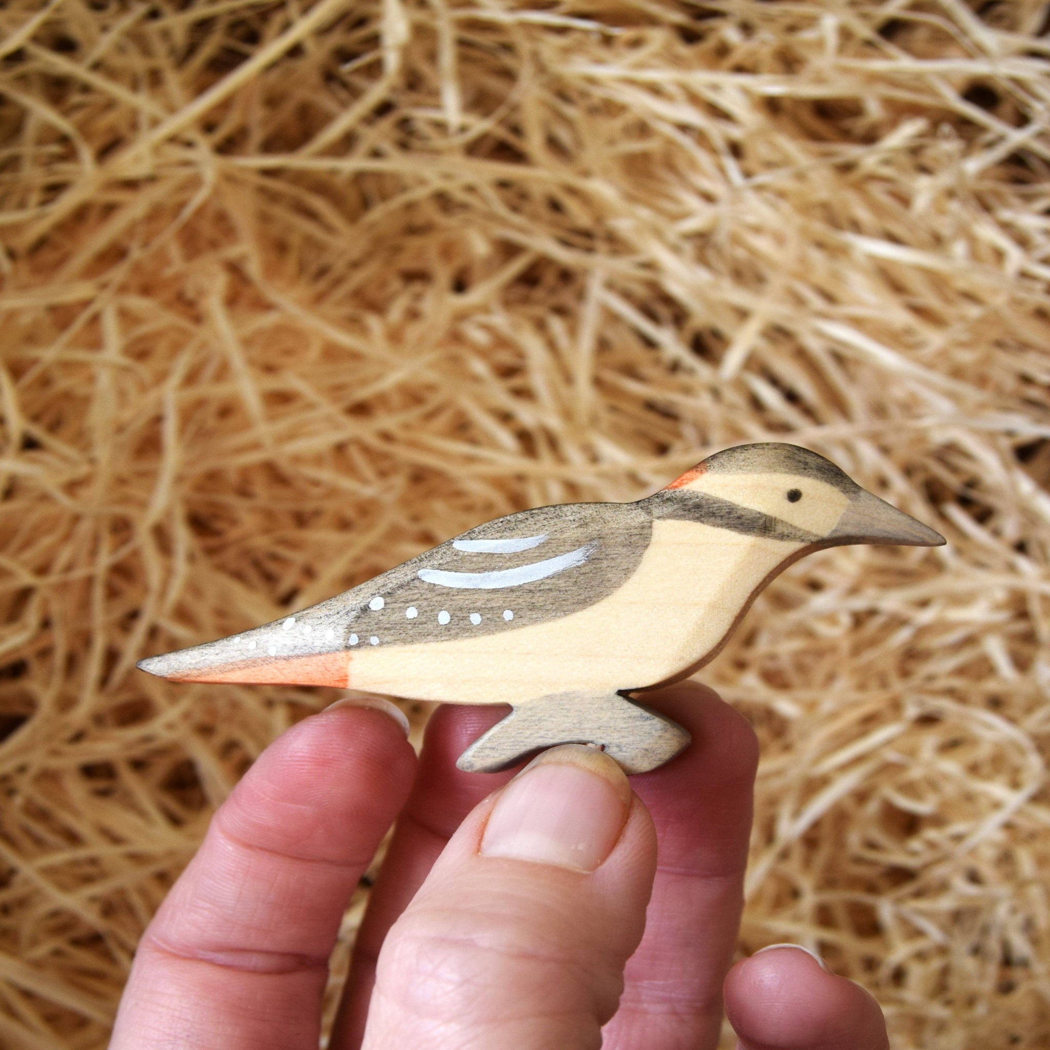 Hand holding a wooden bird figurine against a straw background