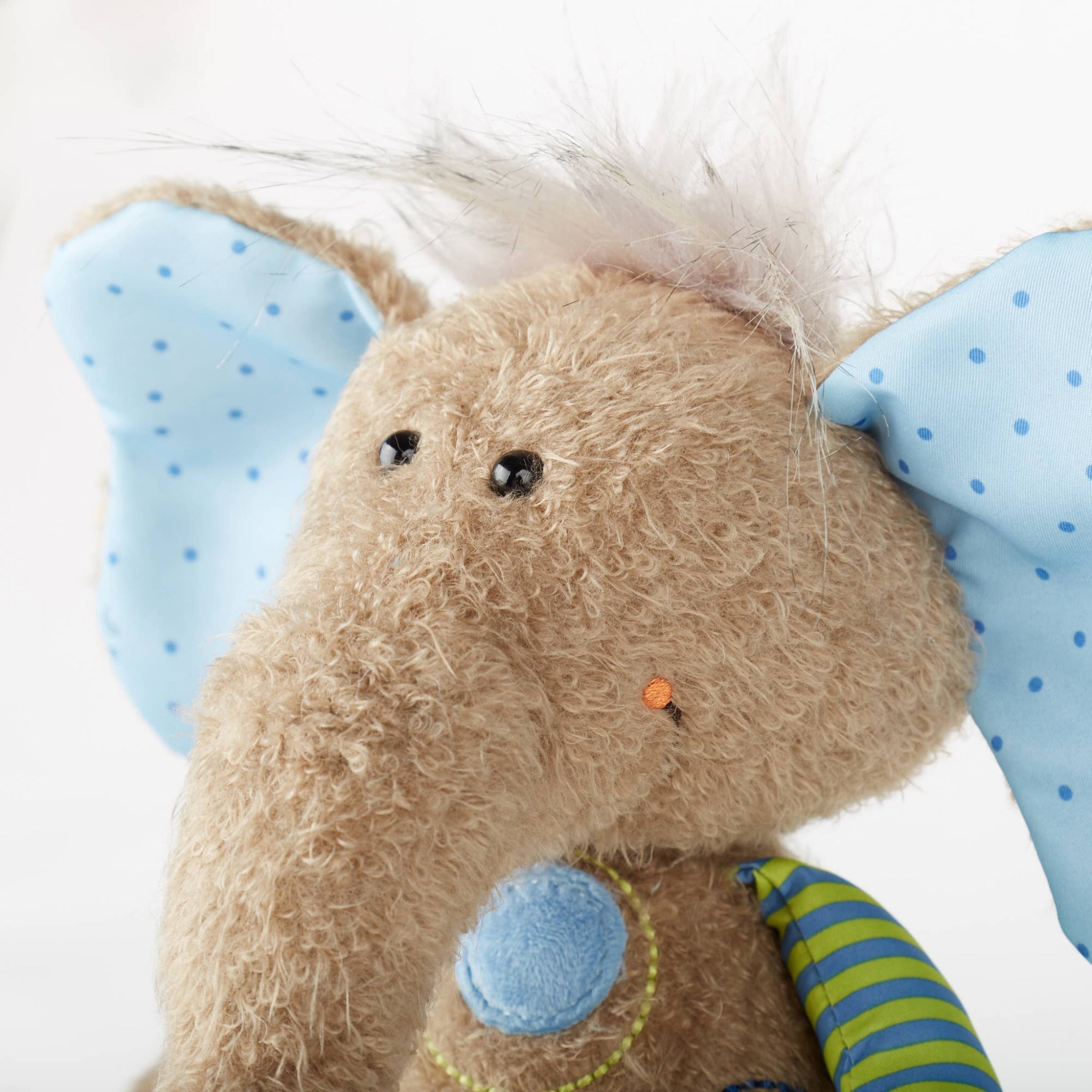 Close-up of a plush elephant toy with blue ears and a striped tail on a white background