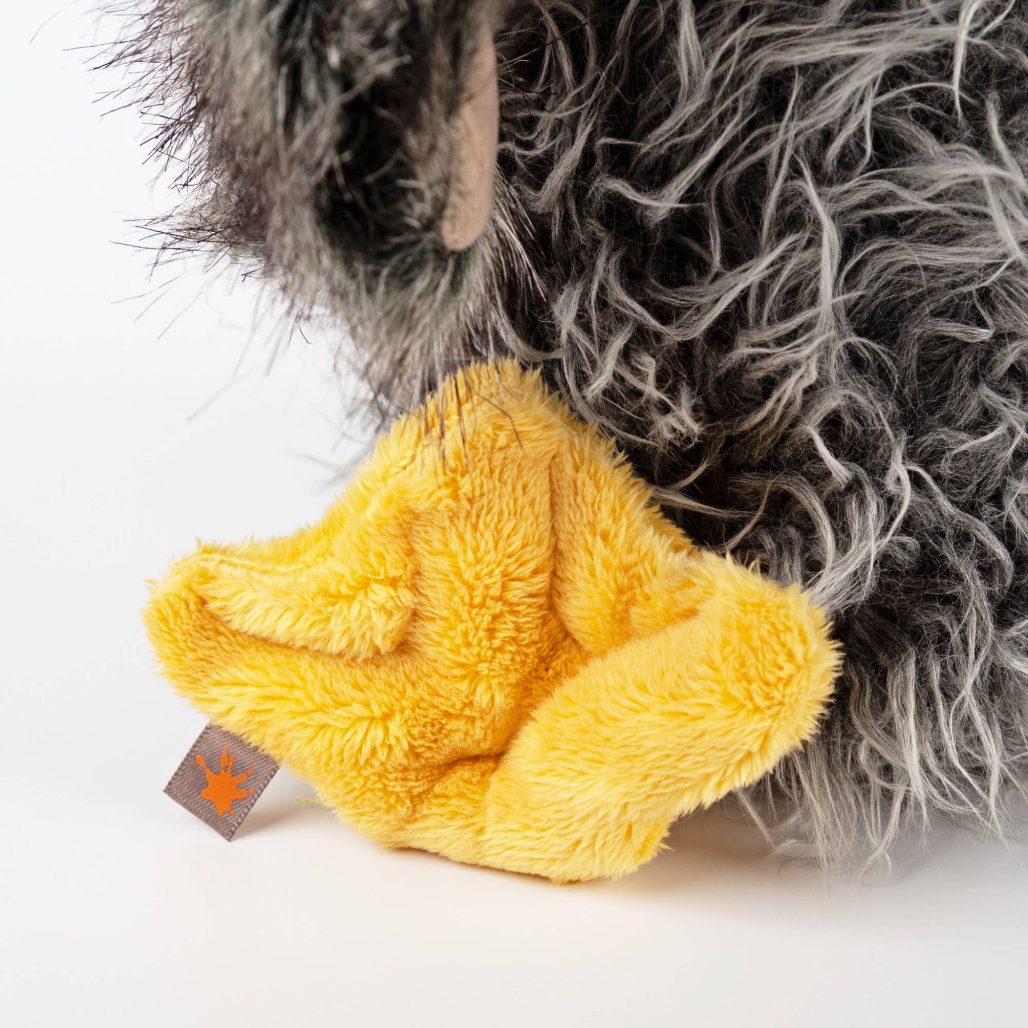 Close-up of a plush toy with a yellow paw and gray fur, on a white background.