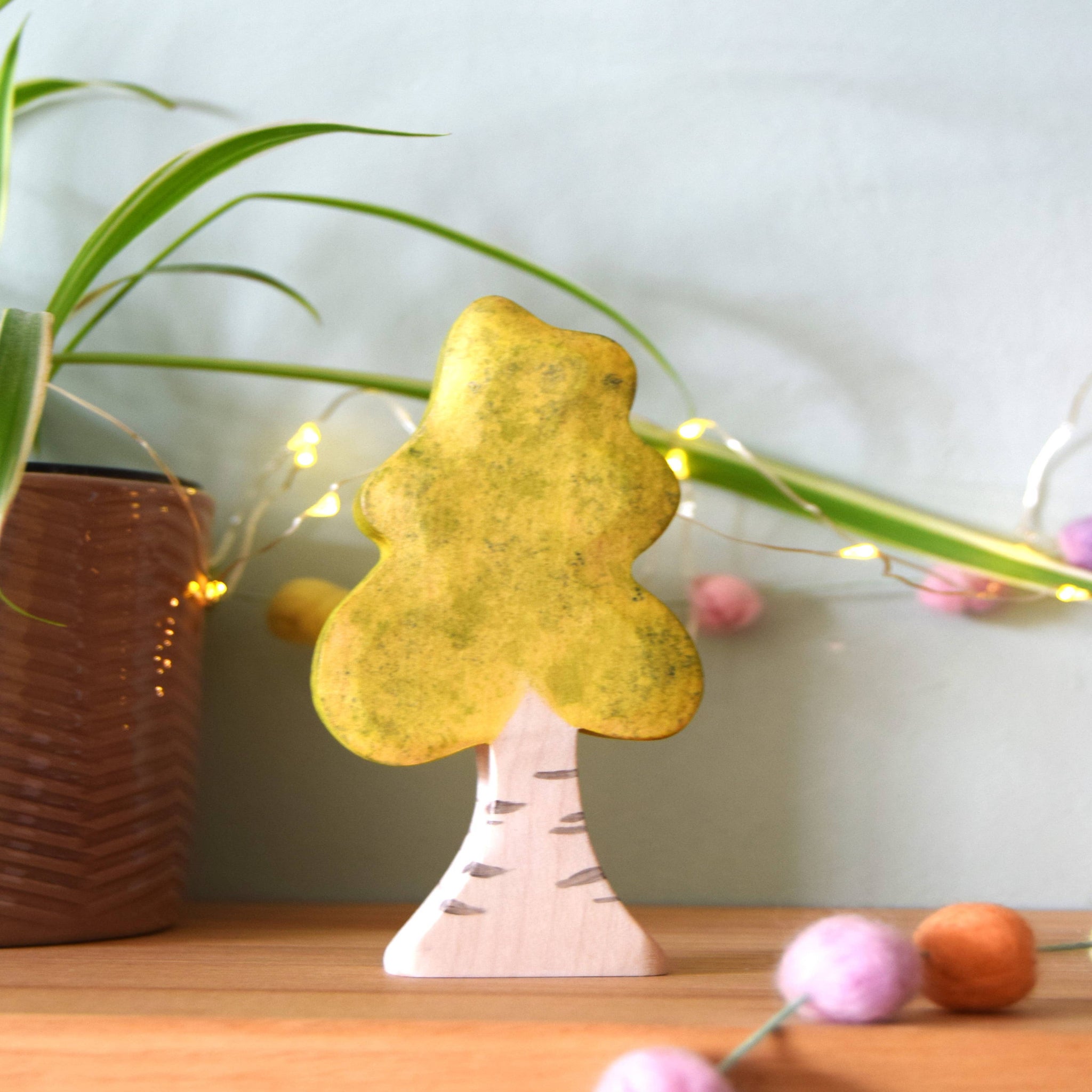 Decorative tree-shaped object on a wooden surface with plants and lights in the background