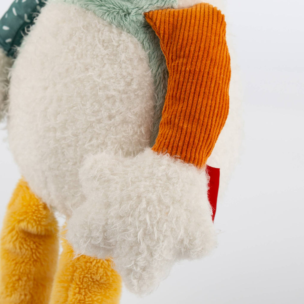 Close-up of a plush toy with a white body, orange arm, and yellow legs on a white background.