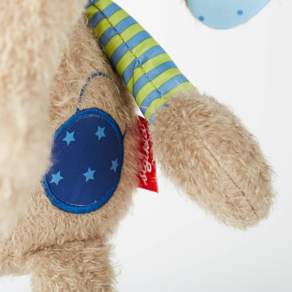 Close-up of a teddy bear with a blue paw patch and striped arm on a white background