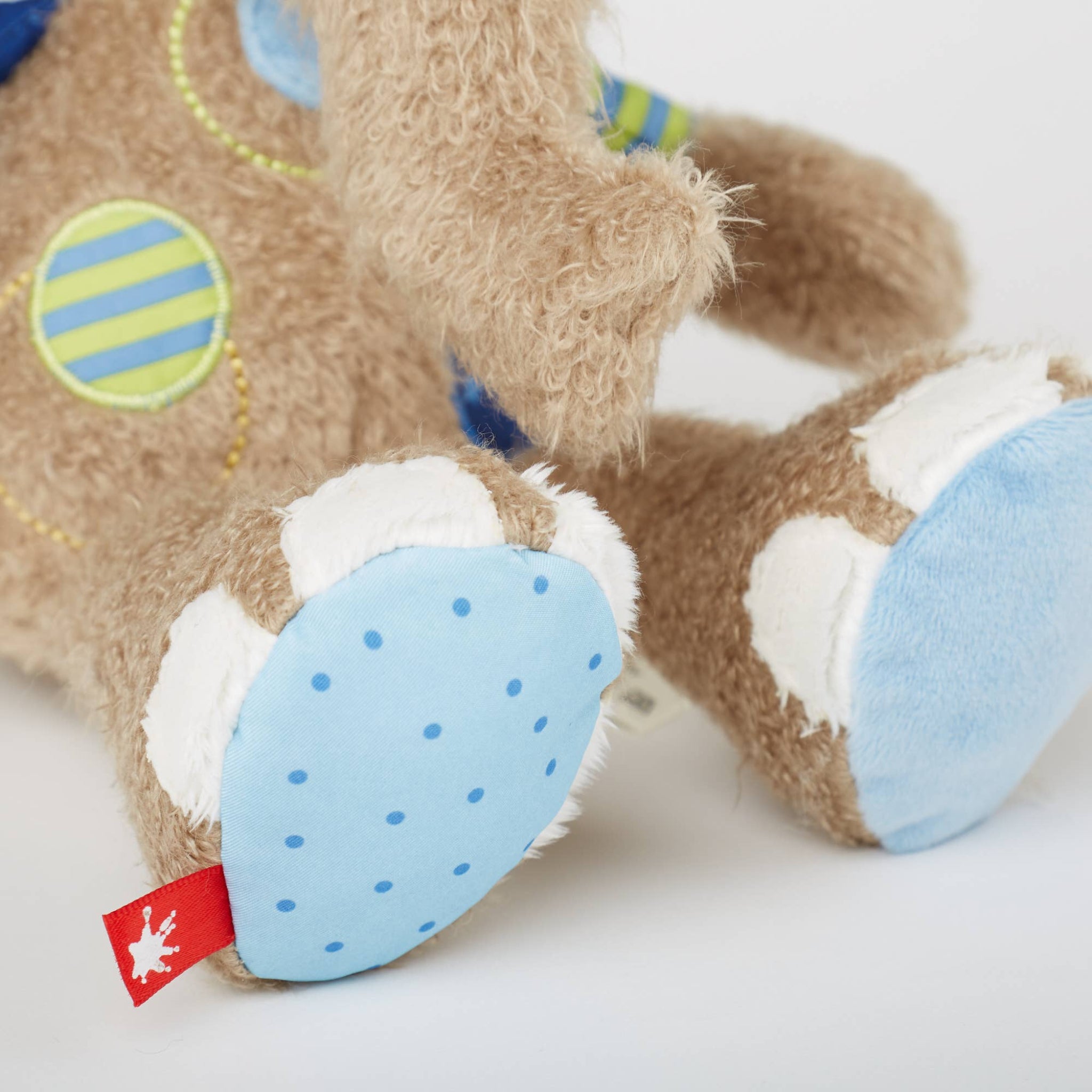 Close-up of a plush toy with blue paw pads and a red tag on a white background