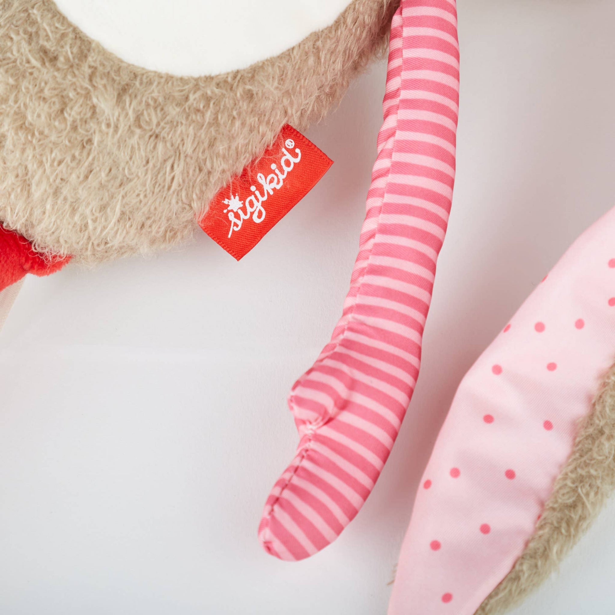 Close-up of a plush toy with pink and red striped and polka dot elements, featuring a Stiglitz label.