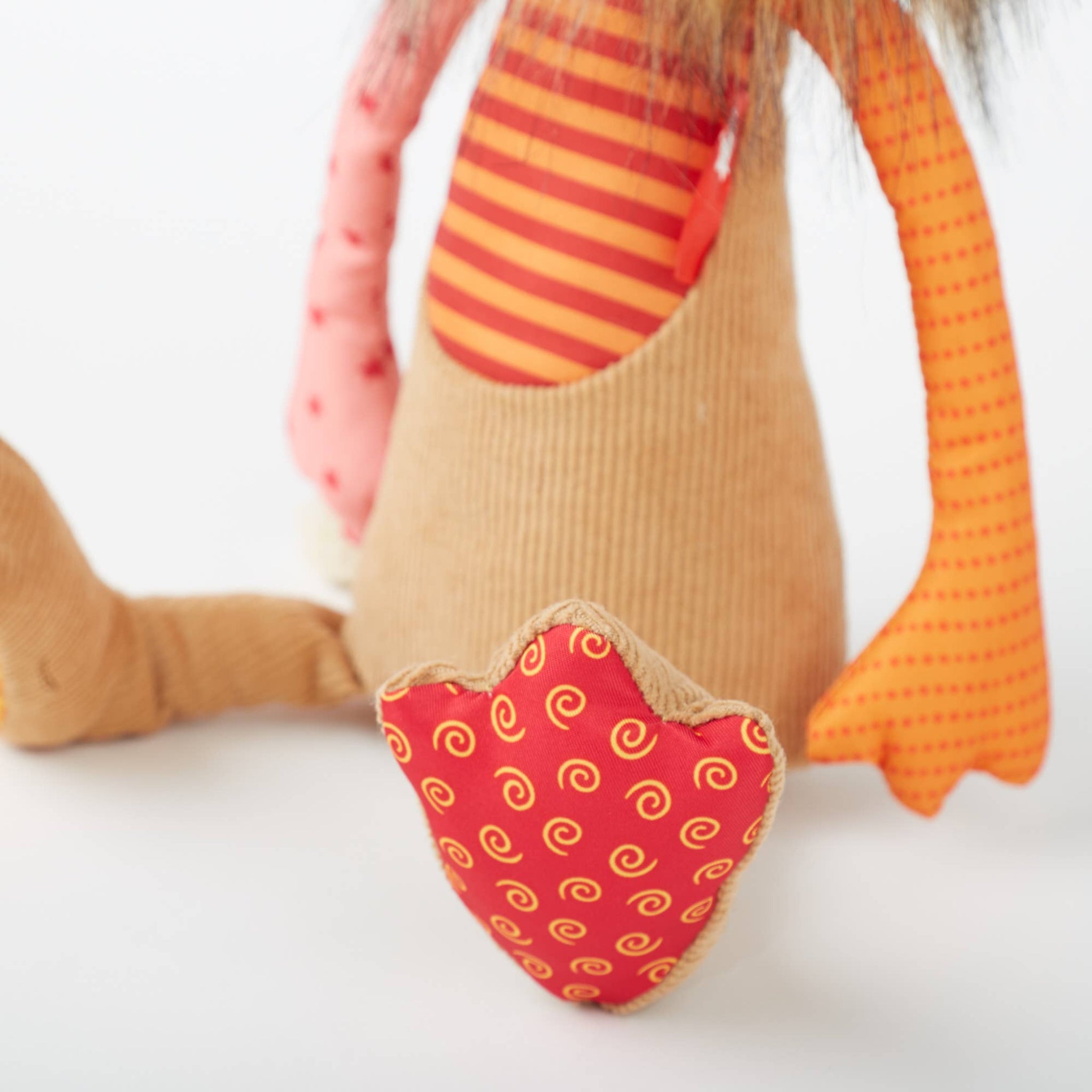 Close-up of a plush toy with orange and red patterned elements on a white background